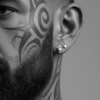 close-up flame skull earrings on rugged biker man with beard and face tattoos