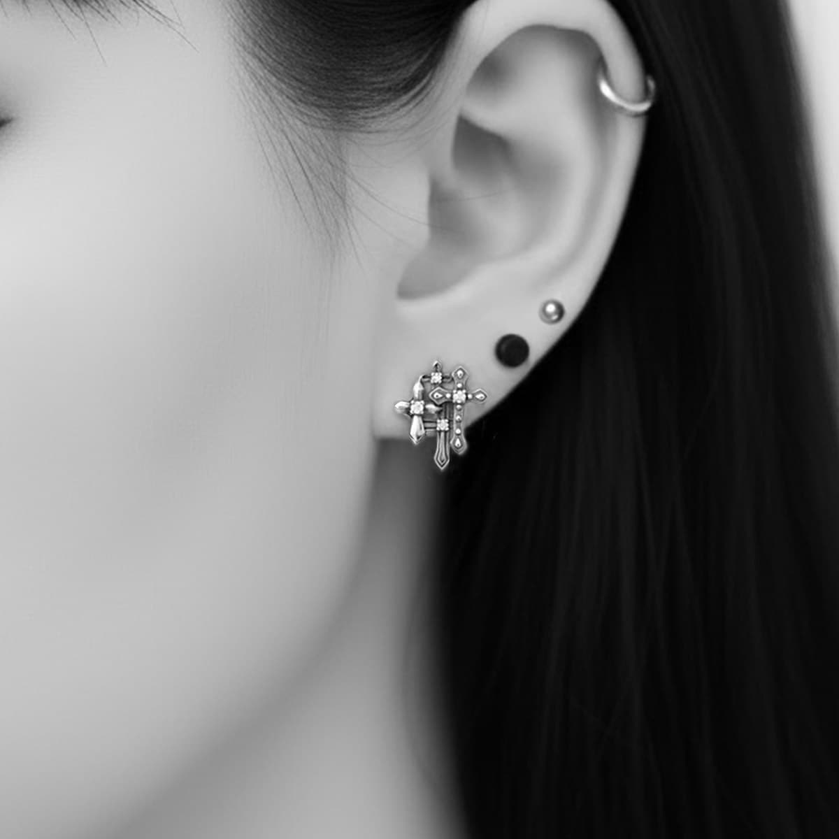 darkened silver gothic cross earrings in ear of goth girl  with multiple piercings 