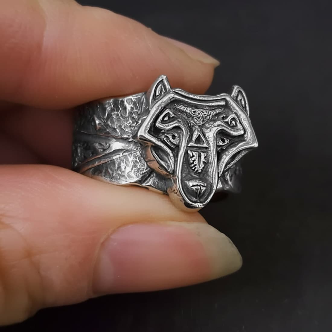 handmade norse viking wolf ring held between models fingers to show the wide chunky band