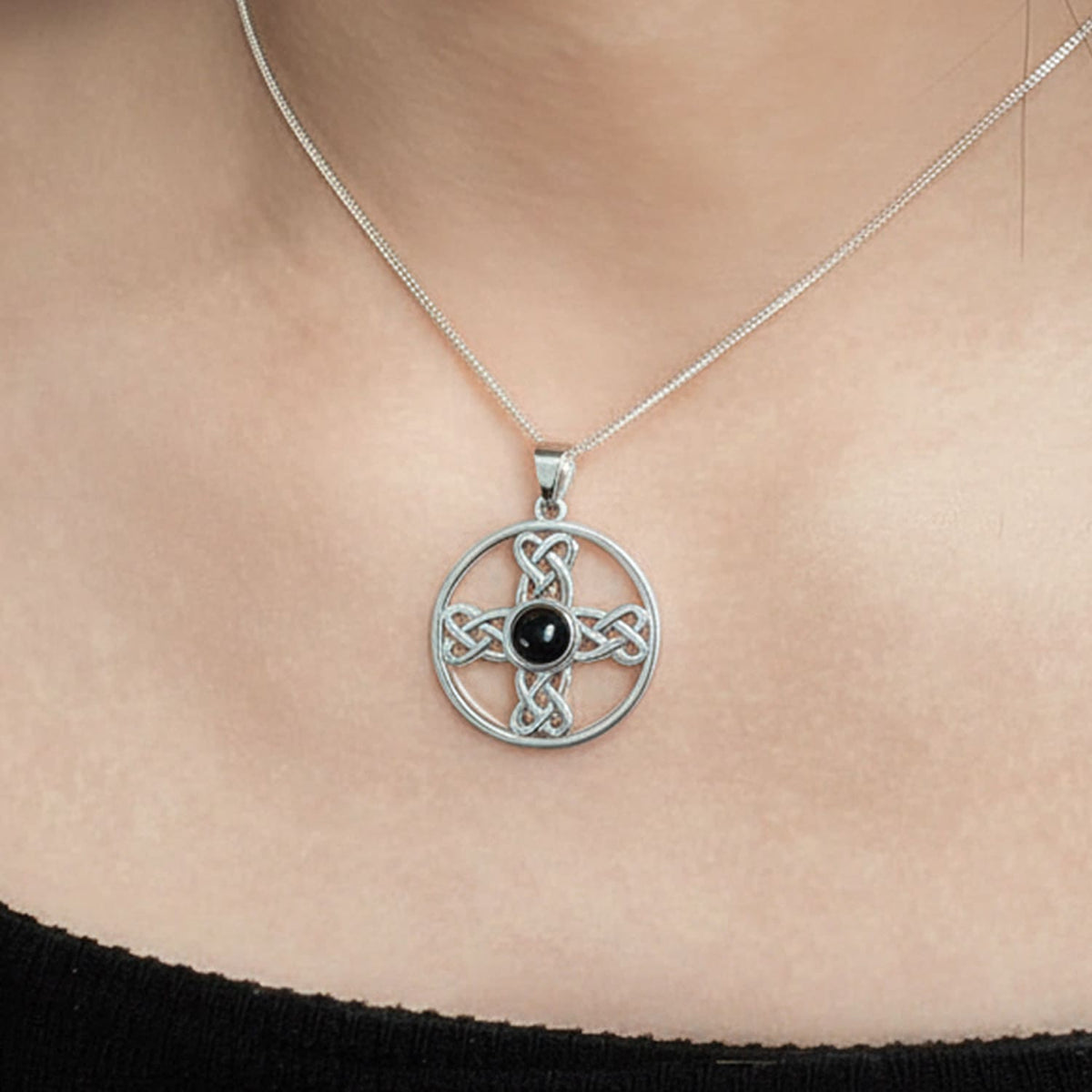A sterling silver Celtic knot cross pendant necklace with a central black onyx gemstone, shown worn on a model's neck.