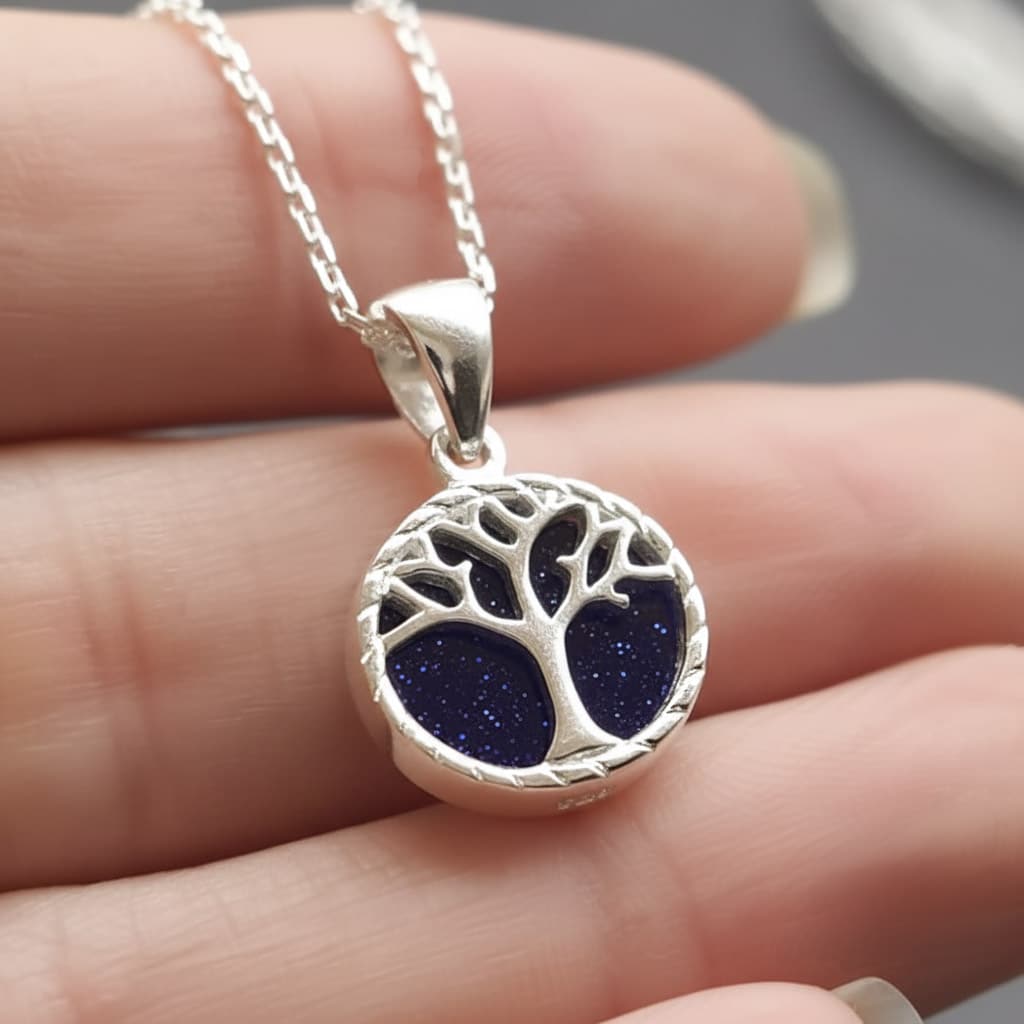 close-ip of small round blue goldstone tree of life necklace resting in a models hand