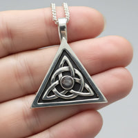 silver handmade trinity knot pendant with hematite stone and sterling curb chain held against a hand for size perspective 