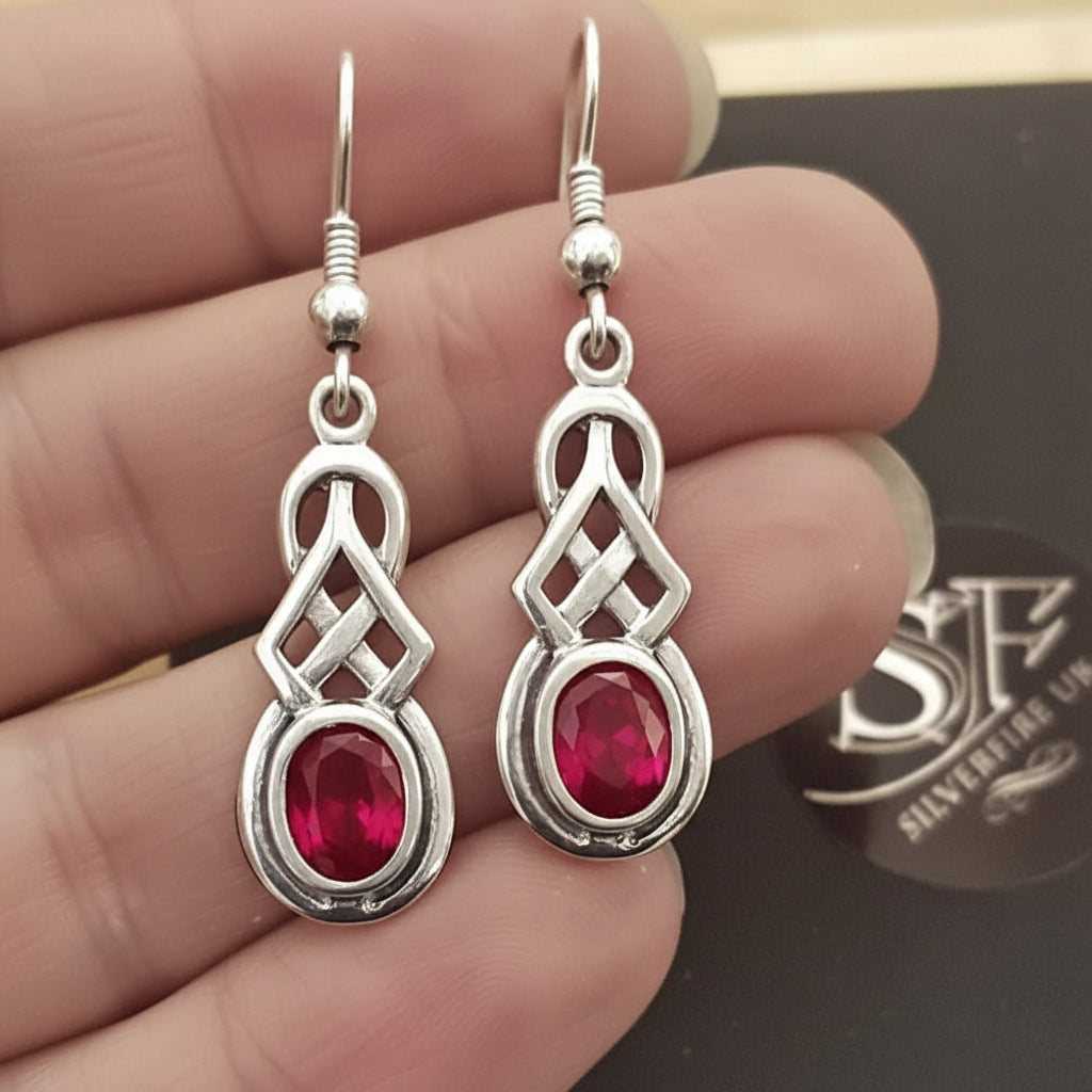 Sterling silver Celtic ruby dangle earrings in hand of a model
